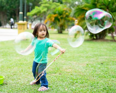 Parkta sabun köpüğüyle oynayan sevimli aktif Asyalı kız.