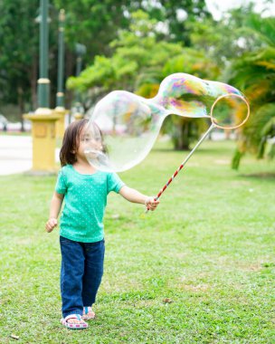 Parkta sabun köpüğüyle oynayan sevimli aktif Asyalı kız.