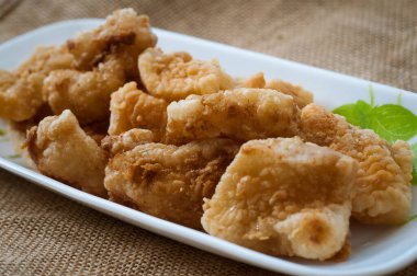 Malezya usulü dövülmüş ve kızartılmış dory balığı küpleri. Kahverengi arka planda uzun bir tabakta servis edilmiş.