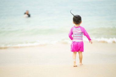 Mutlu Asyalı çocuk sahilde koşuyor.