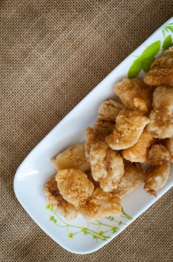 Malezya usulü dövülmüş ve kızartılmış dory balığı küpleri. Kahverengi arka planda uzun bir tabakta servis edilmiş.