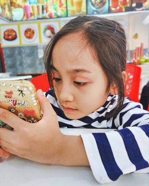 Malezya, Bangi - 7 Eylül 2024 Restoranda cep telefonu kullanan küçük kız.