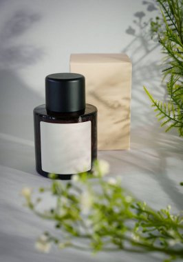 Estetik arka planla çevrili Karanlık Parfüm Şişesi, parfüm markaları ve güzellik kampanyaları için mükemmel minimalist hayat. Üzerinde boş etiket olan koyu renk bir parfüm şişesi.