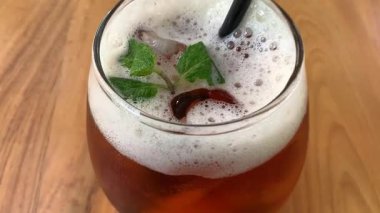 Yuvarlak bardakta soğuk buzlu çay köpüklü ve taze naneli, siyah pipetli. Davetkar ve sıradan, yaz kafesi ya da yaşam tarzı tasviri için mükemmel, naneli ve köpüklü buzlu çay bardağı tazeleme