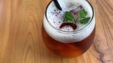 Yuvarlak bardakta soğuk buzlu çay köpüklü ve taze naneli, siyah pipetli. Davetkar ve sıradan, yaz kafesi ya da yaşam tarzı tasviri için mükemmel, naneli ve köpüklü buzlu çay bardağı tazeleme