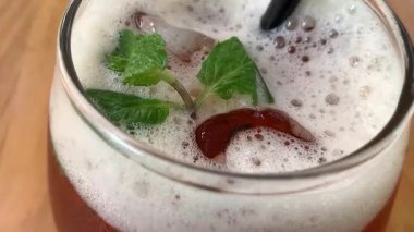Yuvarlak bardakta soğuk buzlu çay köpüklü ve taze naneli, siyah pipetli. Davetkar ve sıradan, yaz kafesi ya da yaşam tarzı tasviri için mükemmel, naneli ve köpüklü buzlu çay bardağı tazeleme