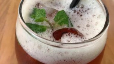 Yuvarlak bardakta soğuk buzlu çay köpüklü ve taze naneli, siyah pipetli. Davetkar ve sıradan, yaz kafesi ya da yaşam tarzı tasviri için mükemmel, naneli ve köpüklü buzlu çay bardağı tazeleme