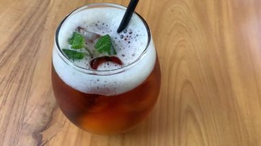 Yuvarlak bardakta soğuk buzlu çay köpüklü ve taze naneli, siyah pipetli. Davetkar ve sıradan, yaz kafesi ya da yaşam tarzı tasviri için mükemmel, naneli ve köpüklü buzlu çay bardağı tazeleme