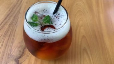 Yuvarlak bardakta soğuk buzlu çay köpüklü ve taze naneli, siyah pipetli. Davetkar ve sıradan, yaz kafesi ya da yaşam tarzı tasviri için mükemmel, naneli ve köpüklü buzlu çay bardağı tazeleme