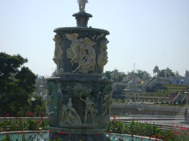 Heykelleri, su birikintisi, renkli ağaçları ve çiçekleri olan büyük yuvarlak bir yapı.