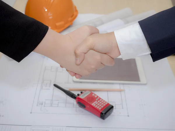 Handshake of two business women over the Architect plan and tabl