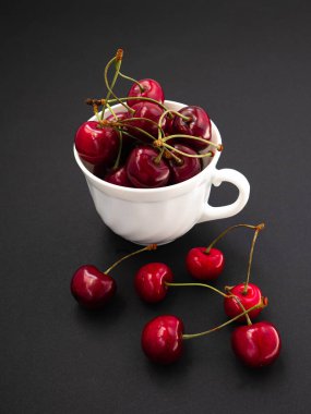 Tatlı kirazlar, beyaz bardakta, siyah arka planda.
