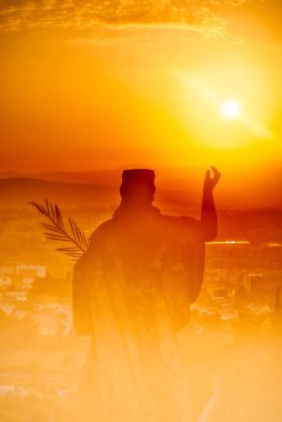 Gün batımında palmiye dalı olan bir kadının heykeli ve altında inanç ve barışın sembolü olan bir şehrin manzarasının soyut görüntüsü.