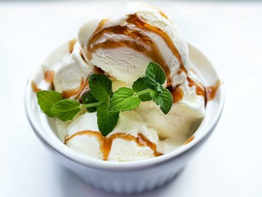 A serving of vanilla ice cream on a plate topped with caramel and mint. 