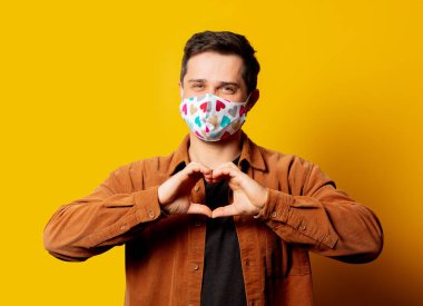 Yüz maskeli adam sarı arka planda kalp hareketi gösteriyor. 