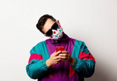 Eşofmanlı ve beyaz arka planda cep telefonu olan güneş gözlüklü bir stil adamı.