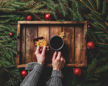 Kadın eli çay bardağını kurabiye ve Noel ağacının yanında tutar.