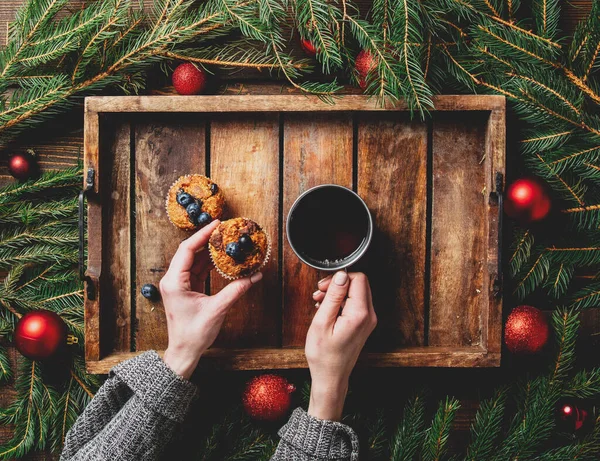 Vrouwelijke Handen Houden Kopje Thee Naast Kerstboom Muffins Een Tafel — Stockfoto