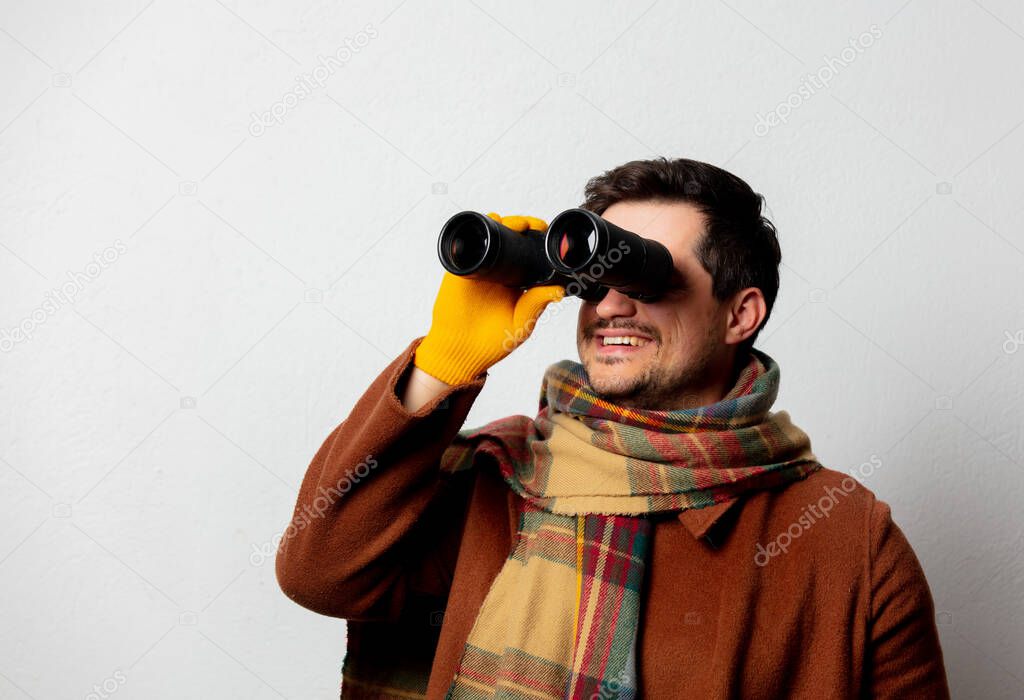 Style man in coat and scarf watch in a binoculars on white background