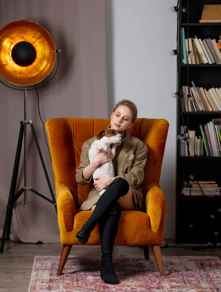 Style blonde in vintage clothes with a dog in an armchair at home