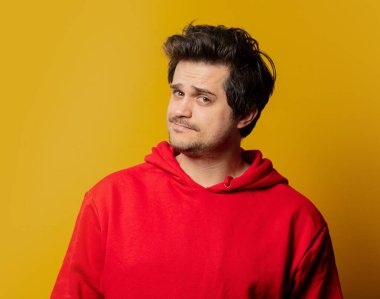 Sarı arka planda kırmızı kazaklı, şaşkın adam. 