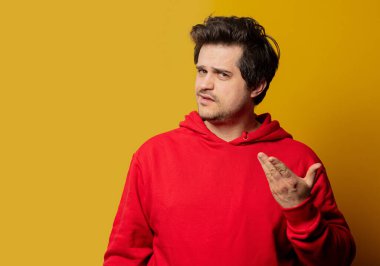 Sarı arka planda kırmızı kazaklı, şaşkın adam. 