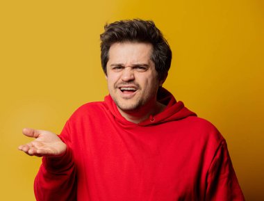 Sarı arka planda kırmızı kazaklı, şaşkın adam. 