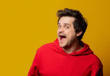 Sarı arka planda kırmızı kazaklı, beyaz, gülümseyen adam.