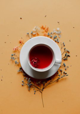 Sarı arka planda kuru çiçekler olan bir fincan çay. Görünümün üstünde 