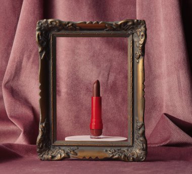 Red lipstick in a photo frame on burgundy color fabric background 