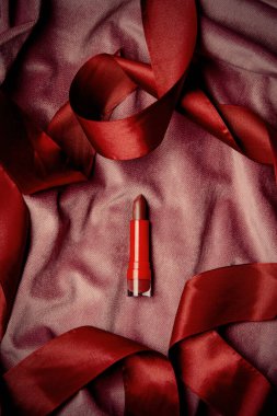 Red lipstick on burgundy color fabric background, top view 