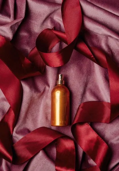 Golden perfume bottle and red ribbon arond on burgundy color fabric background 