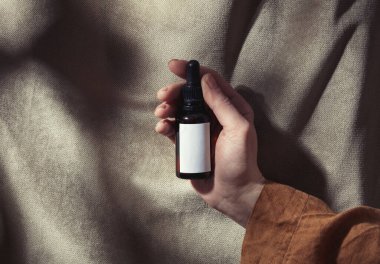 Kadın eli, kumaş arka planında siyah bir şişe tutuyor. 