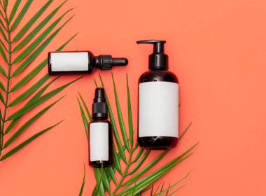 Pembe arka planda üç kozmetik şişe ve palmiye yaprağı. Görünümün üstünde