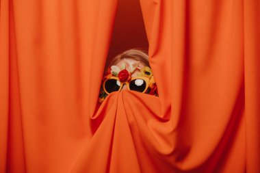 Güneş gözlüklü ve çiçekli kadın turuncu perdelerde saklanıyor.