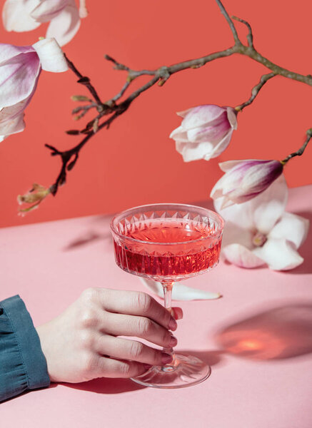 Женщина держит стакан с напитком рядом с веткой магнолии на оранжевом фоне 