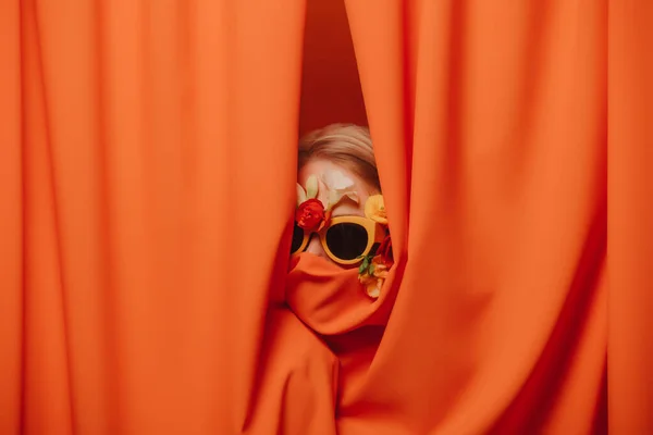 Vrouw Zonnebril Bloemen Verbergen Zich Oranje Gordijnen — Stockfoto