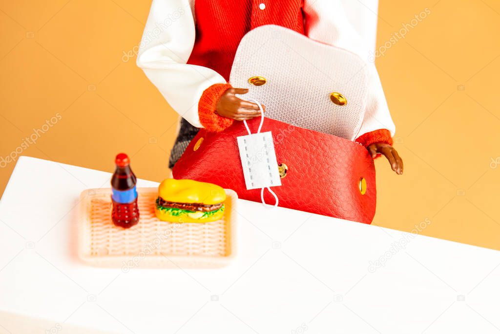 african-american female doll hand hold mask next to fastfood on a table