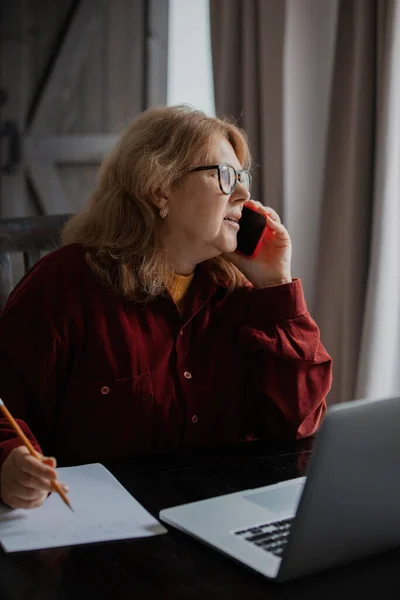 Ηλικιωμένη Γυναίκα Κάθεται Στον Υπολογιστή Και Μιλάει Τηλεφωνικώς — Φωτογραφία Αρχείου