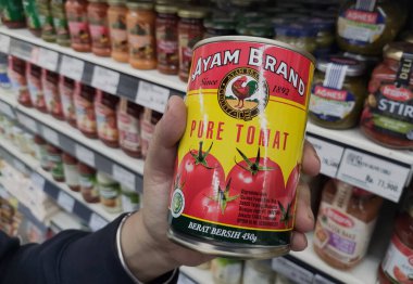 Domates püresi kutularını tutan ellerin yakın çekimi, süpermarket arka planında raflarda markalı tavuk ürünleri.