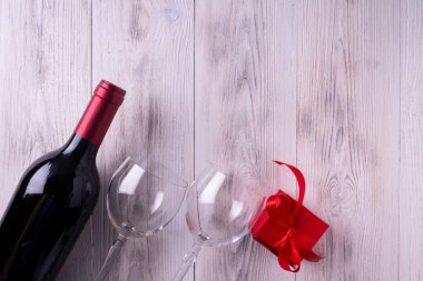 Bir şişe alkol, şarap bardakları, kırmızı kutuda bir hediye. Beyaz ahşap bir arka planda. Metin için boşluk.