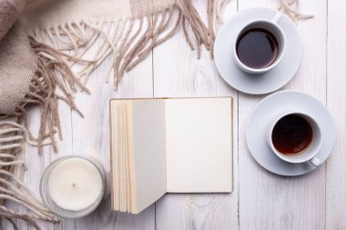 İki fincan sade kahve, bir mum, açık bir defter, bej renkli yün bir ekose. Beyaz ahşap bir arka planda. Rahat ol. Boşluğu kopyala.