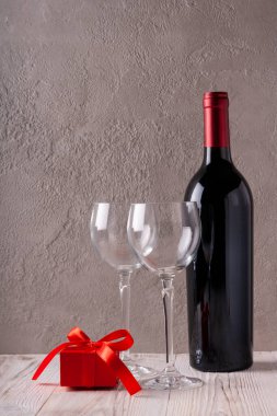 Bir şişe kırmızı şarap ve tatmak için iki şarap bardağı. Alçının arka planında.