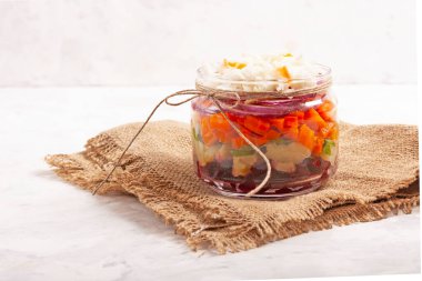 Rus salatası - haşlanmış sebze salatası: patates, pancar, havuç, soğan, lahana turşusu, otlar, ayçiçeği yağı. Gri arkaplanda cam bir kavanozda, yatay yönelimde.