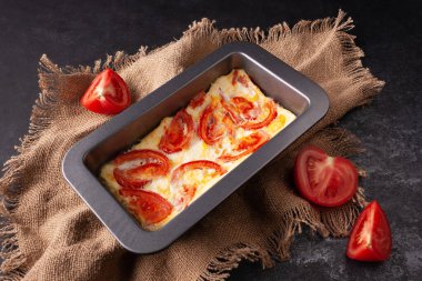 Yumurta ve domatesli omlet, dikdörtgen bir tavada, kumaş kumaştan siyah bir fotoğrafta.