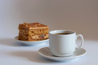 Bir fincan kahveli bir dilim kek ve beyaz arka planda bir fincan çay tabağı.