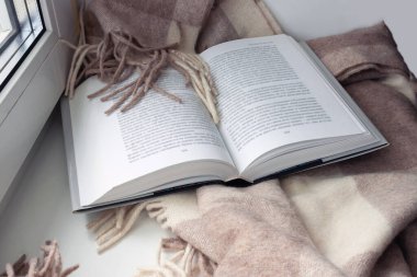 Açık bir kitap, pencere pervazında bir battaniye