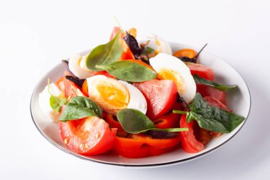 Fesleğenli domates salatası ve beyaz tabakta yumurta.