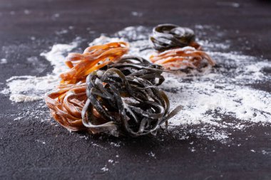 Koyu arkaplanda un olan çiğ ev yapımı makarna. 