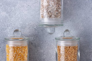 Gri arka planda farklı tipte mısır gevreği olan cam kavanozlar 
